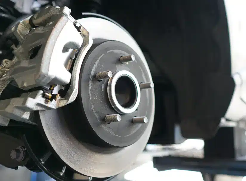 Brake repair at SPES Automotive and Diagnostics. Close-up of a car’s disc brake assembly, showing the brake caliper and rotor, with wheel studs visible; the background is slightly out of focus.