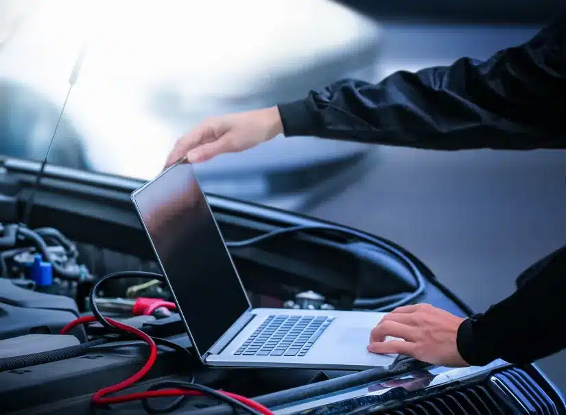 Engine Diagnostics at SPES Automotive and Diagnostics. A person uses a laptop computer on the open hood of a car, with cables connected to the engine, likely diagnosing or repairing the vehicle using automotive diagnostic software.