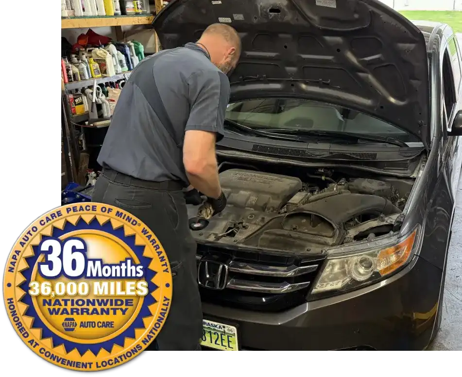 Preventative Maintenance at SPES automotive. A mechanic pours oil into the engine of a gray minivan with its hood open inside an auto repair shop filled with various tools and equipment.